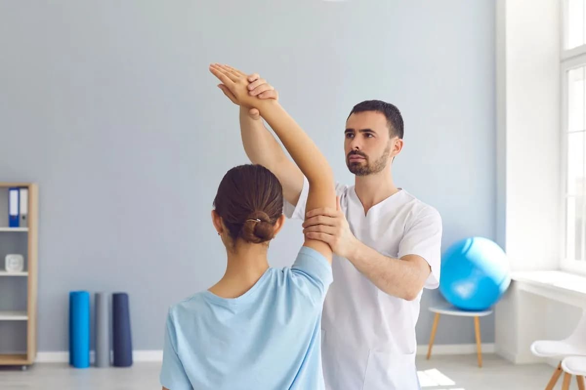 Physiotherapist guiding a woman's raised arm during a shoulder assessment