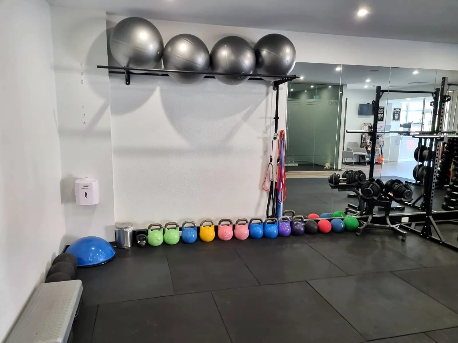 Row of coloured kettlebells and exercise balls along a gym wall
