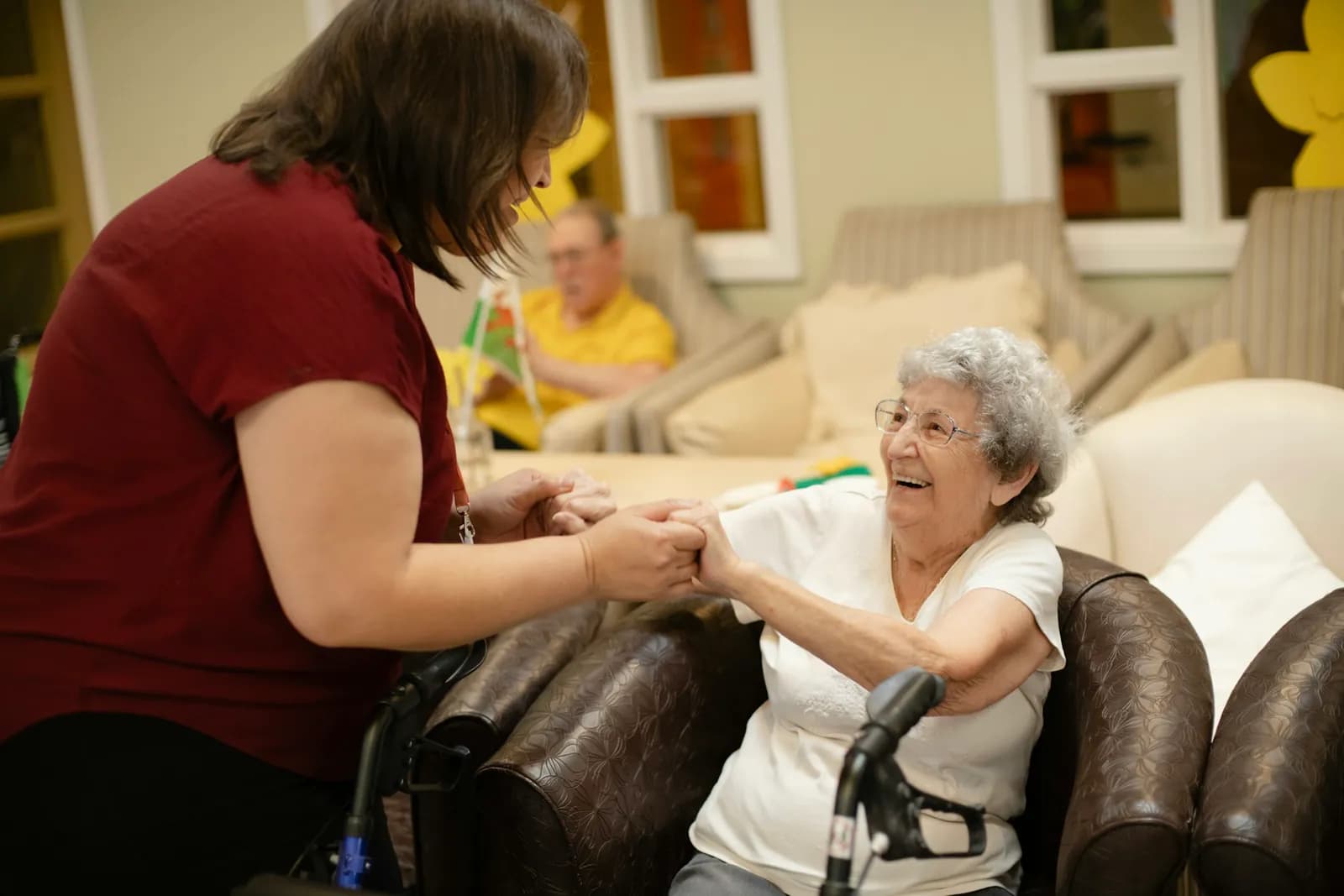 Carer holding an older woman's hands as she gets ready to stand up from her chair