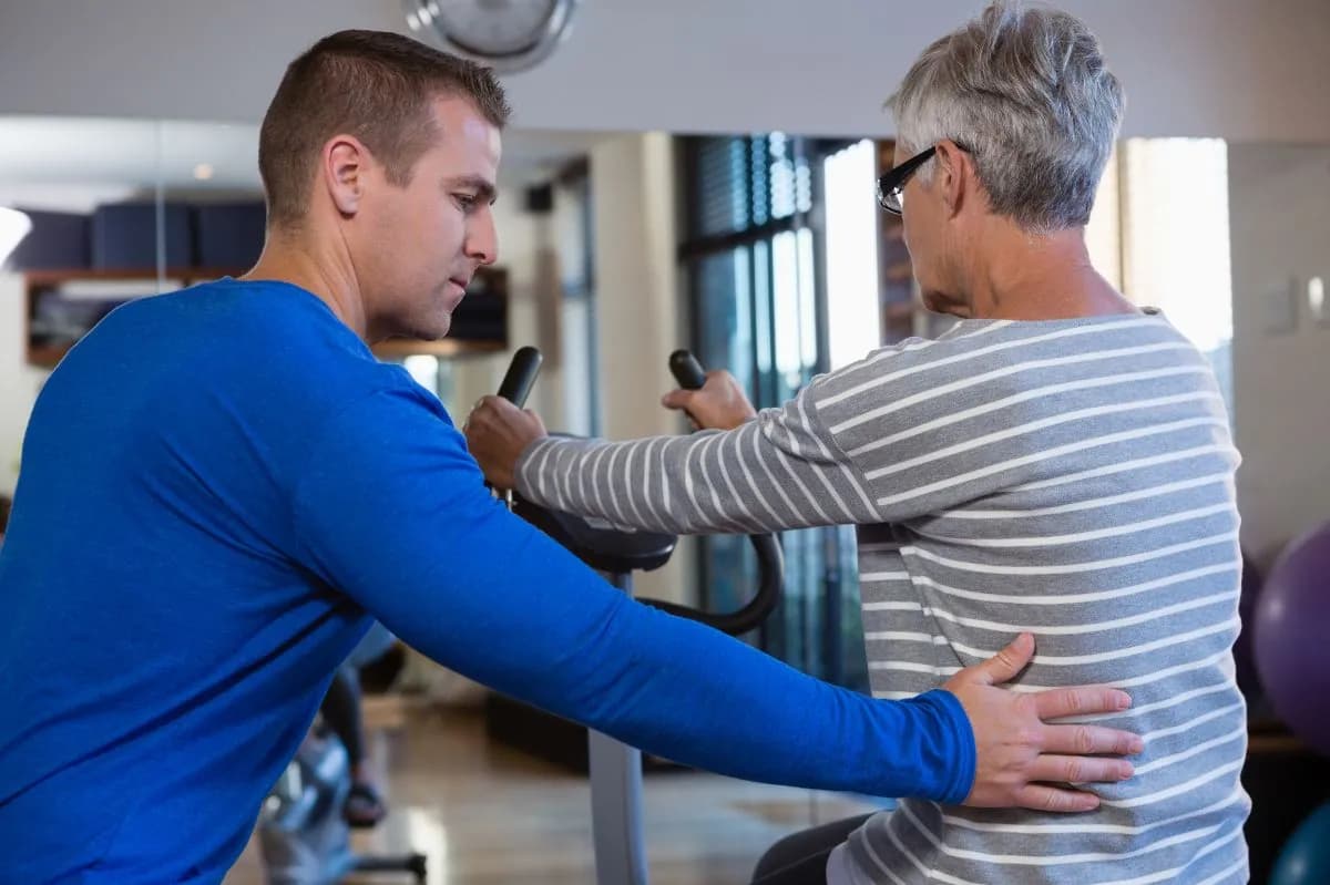 Exercise physiologist supporting an older man through a resistance exercise