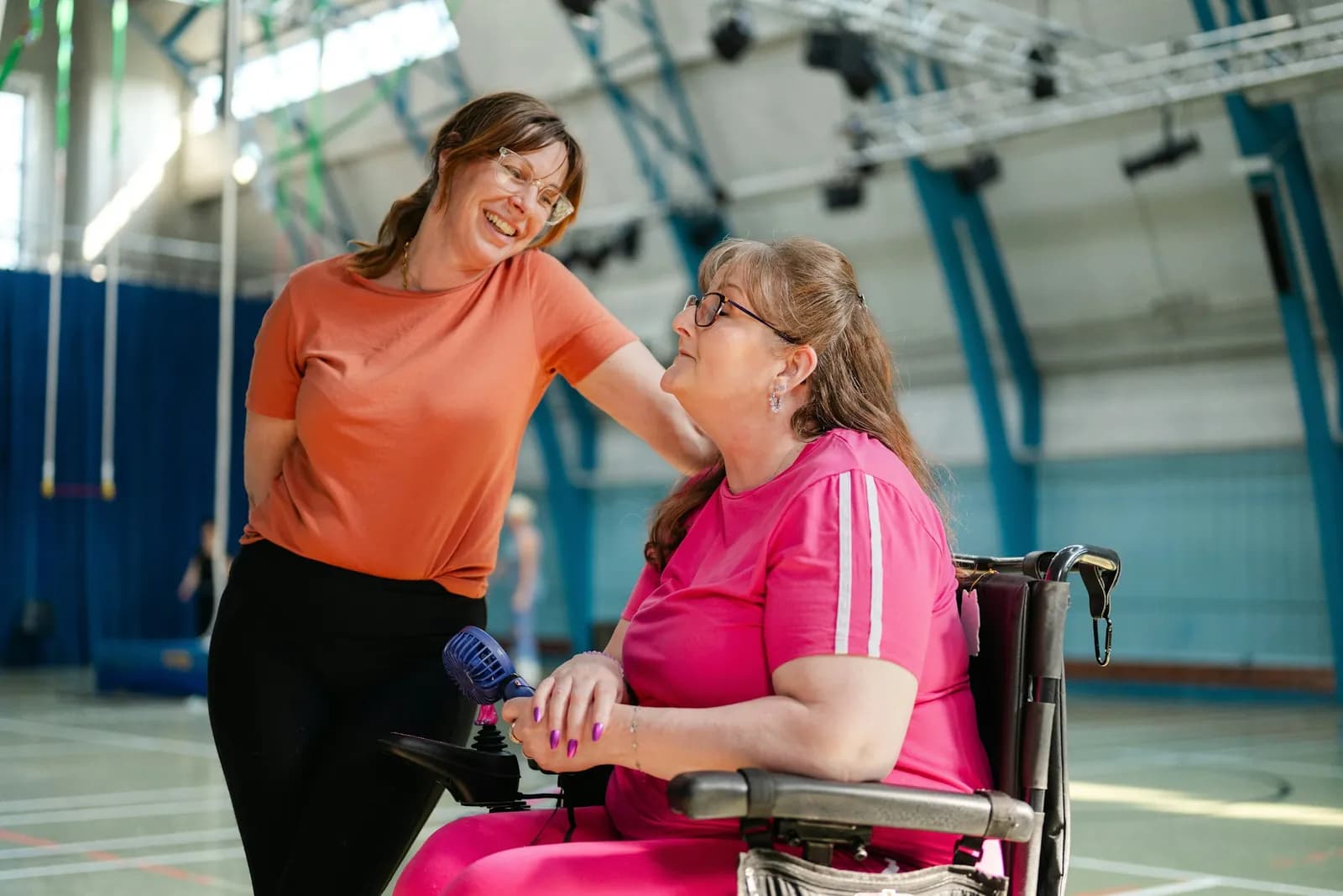 Woman in a wheelchair chatting with her coach in a gym
