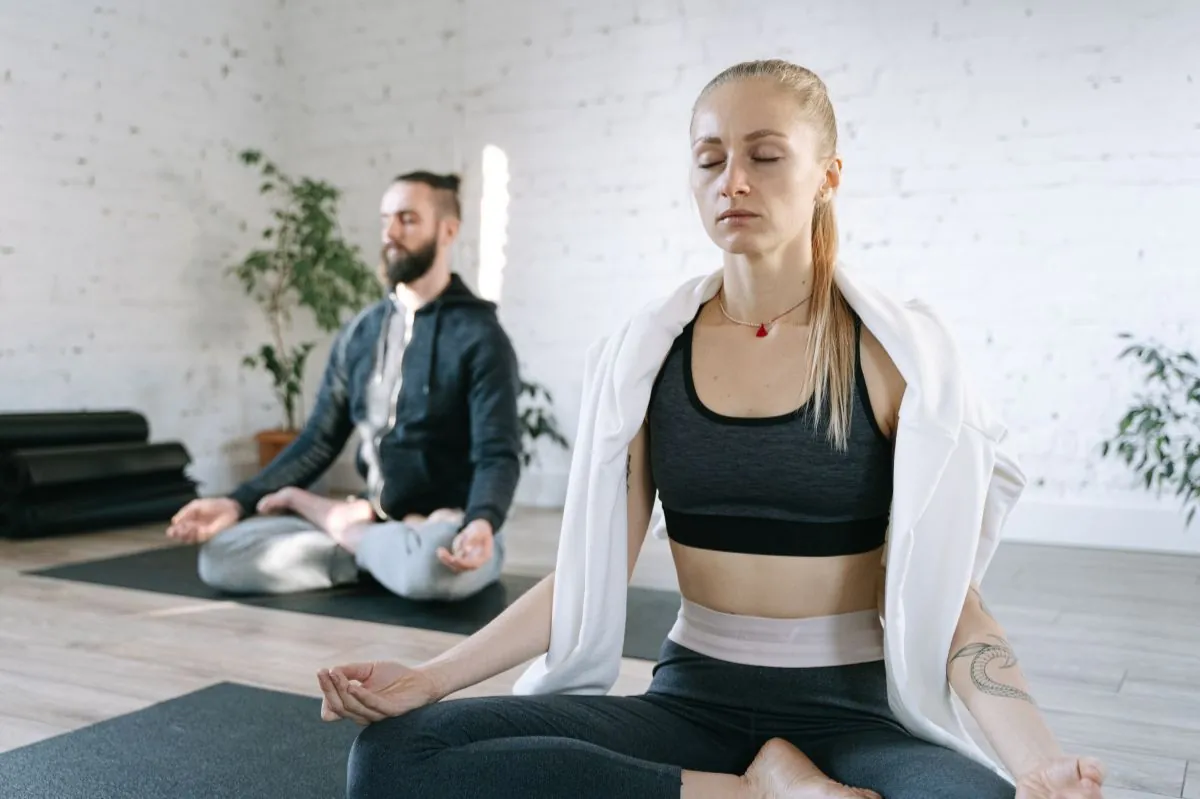 Two people meditating on exercise mats in a bright room