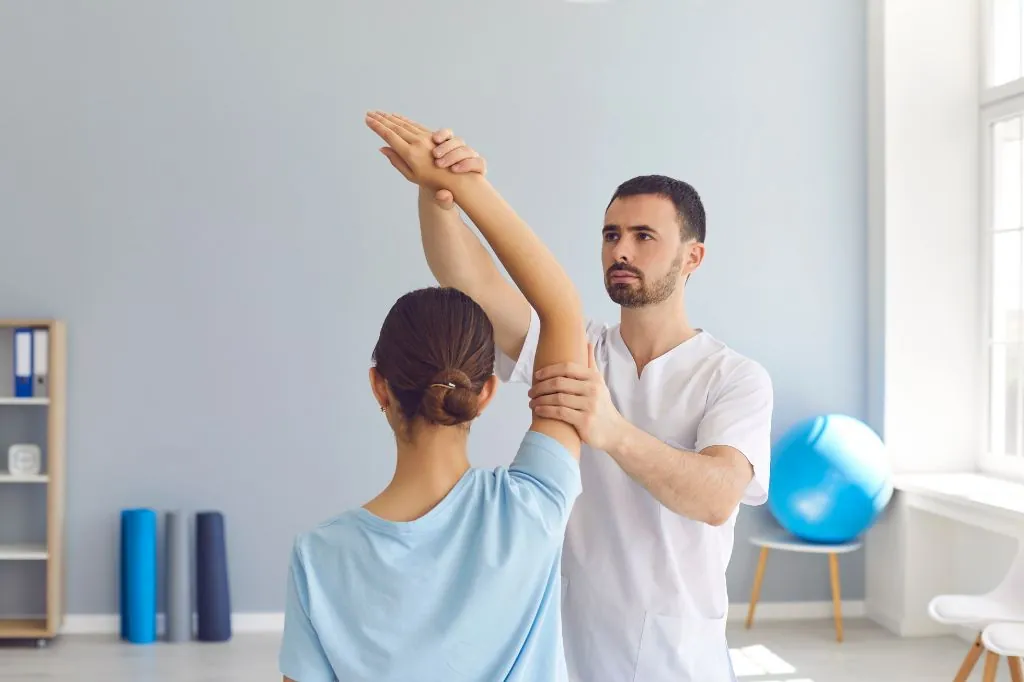 Physiotherapist assisting a woman with an overhead arm stretch