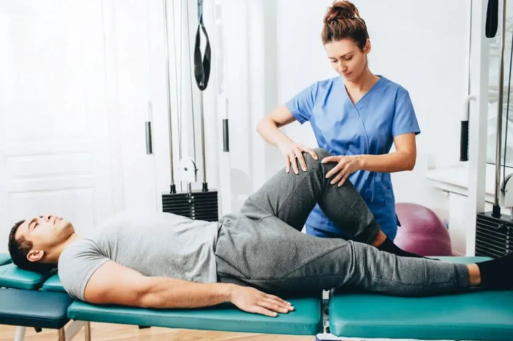Physiotherapist assisting a man with a leg exercise on a treatment table
